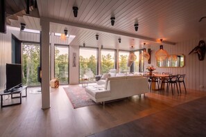 A modern living room with a white sofa, dining table, and chairs, large windows, and a ceiling with exposed beams. - Stay   North - Sundet (Kirkkonummi)