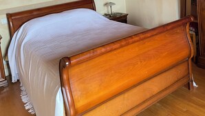 Een houten plafond, een bed met houten frame, een nachtkastje en een lamp.