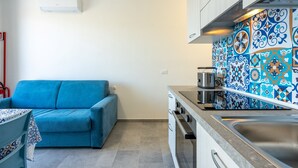 A compact kitchen with a stove, oven, and sink, a blue sofa, and a patterned backsplash. - Affittimoderni Castelsardo - LaRotonda sul Mare (Castelsardo)