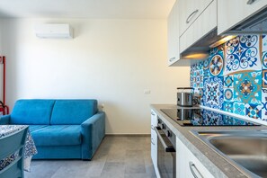 Eine kompakte Küche mit Herd, Backofen und Spüle, ein blaues Sofa und eine gestreifte Spritzschutzwand.