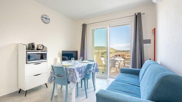 A dining area with a table set for two, a sofa, a microwave, and a TV. - Affittimoderni Castelsardo - LaRotonda sul Mare (Castelsardo)