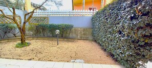 A courtyard with a sandy ground, a tree, a hedge, and a building with a yellow wall and a white fence. - Affittimoderni Viddalba - Mafalda House (Viddalba)