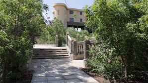 A pathway leading to a building with a curved facade, surrounded by lush greenery and flowering plants. - Amboseli Safari Club (Kimana)