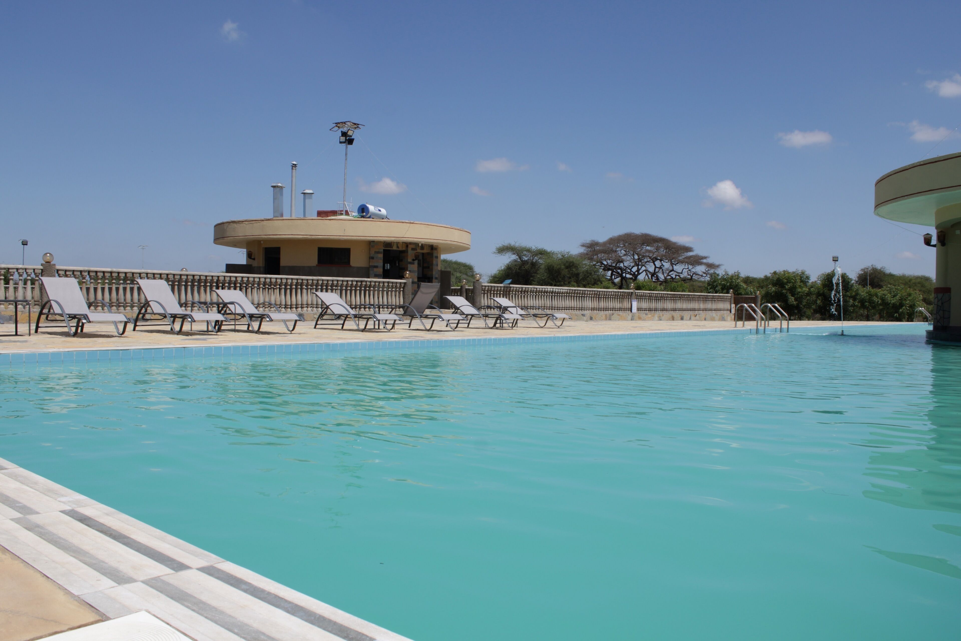A swimming pool with lounge chairs and a building with a circular roof in the background.