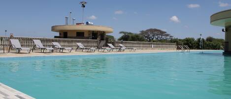 A swimming pool with lounge chairs and a building with a circular roof in the background.