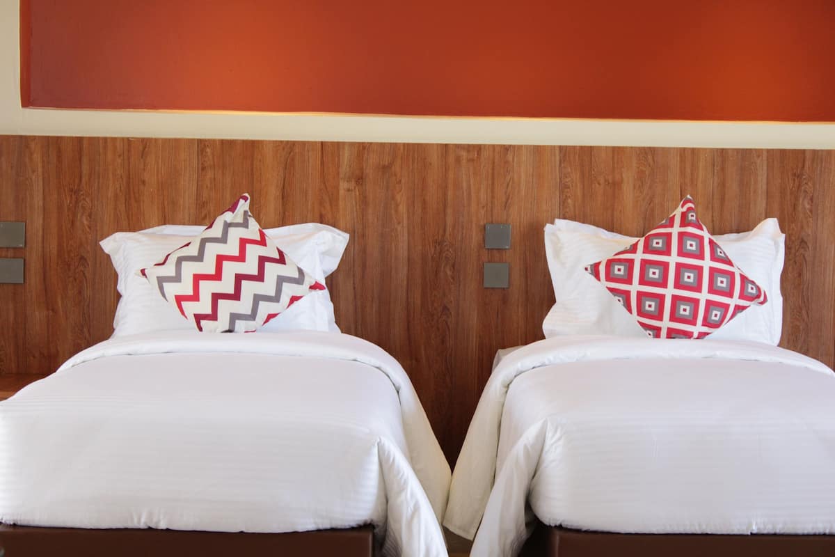 Two beds with white bedding and patterned pillows, a wooden headboard, and a red accent wall.