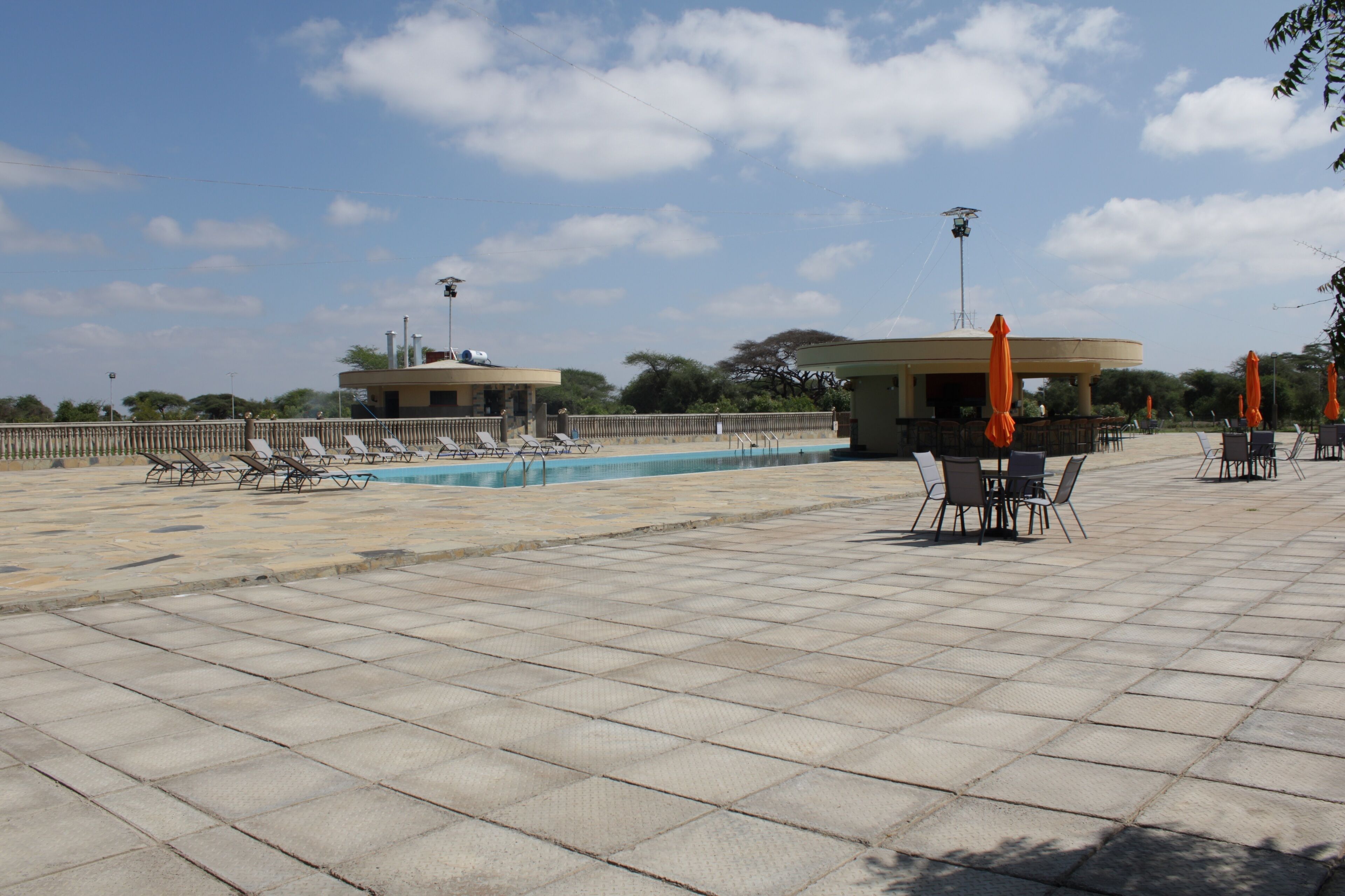 Zona de piscina con sillas de descanso y sombrillas, un área de estar cubierta y cielo despejado.