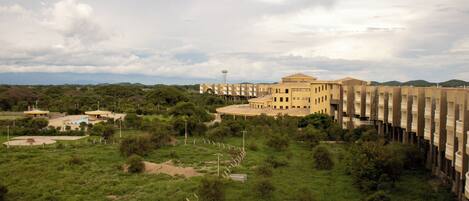 A large building with a central courtyard, surrounded by greenery and a fence.