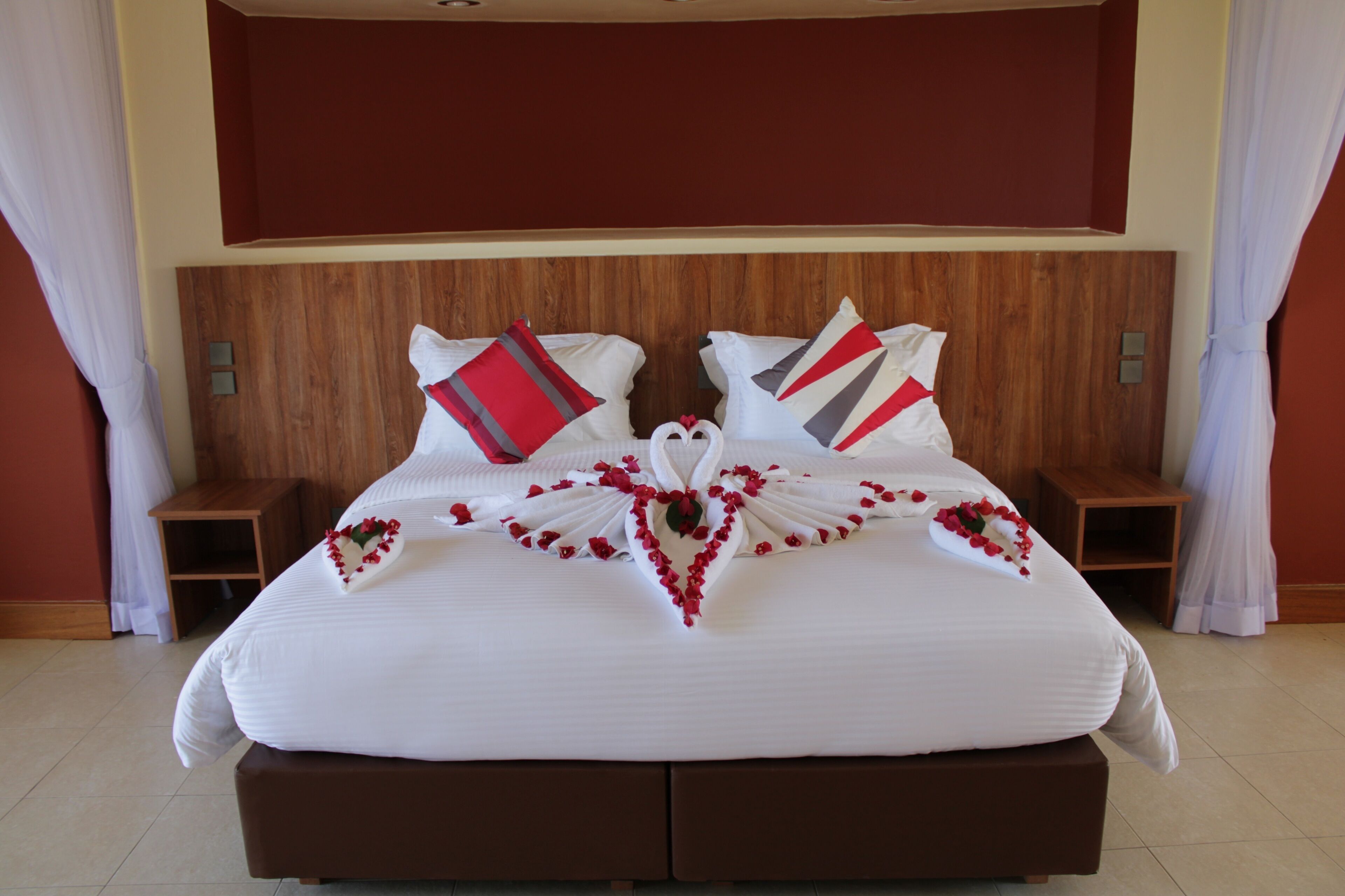 Una cama bien hecha con un arreglo floral en forma de corazón, dos mesitas de noche y un cabecero de madera.