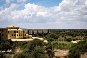 Un edificio grande de color amarillo con varios pisos y techo plano, rodeado de vegetación y árboles.