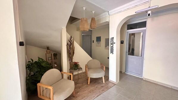 A modern interior with a staircase, two upholstered chairs, a small table with a vase, and a 'welcome' sign.