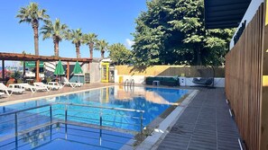 A swimming pool with lounge chairs and umbrellas, a restaurant, and a shaded seating area.