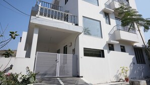 Un edificio blanco de varios pisos con balcones, ventanas amplias y una entrada protegida por una reja.