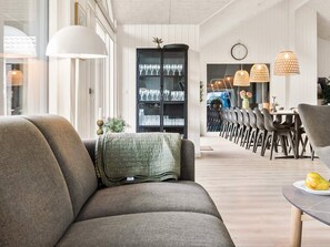 A modern living room with a sofa, dining area with chairs, and a cabinet with glassware. - 5 Star Holiday Home in Idestrup (Idestrup)