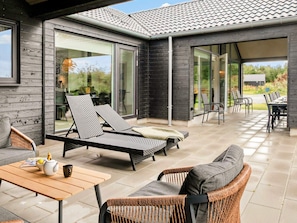 Ein moderner Außenbereich mit Terrasse, Liegestühlen, einem Tisch und einer Essgruppe.