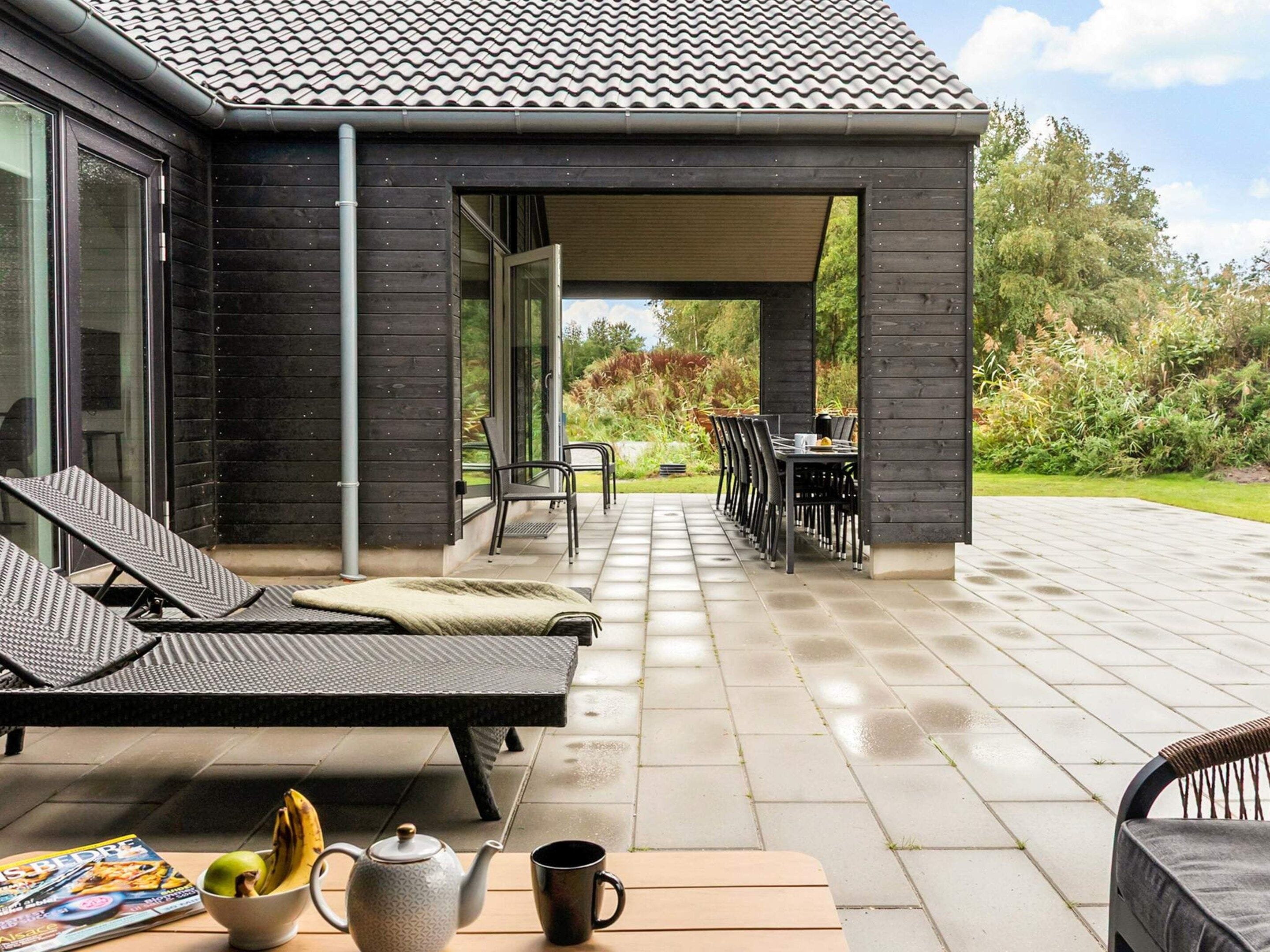 Un espacio de estar al aire libre cubierto con sillones de descanso y una mesa, vista a un jardín y un patio con piso de baldosas.