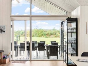 A modern interior with a glass door leading to a grassy outdoor area, a dining table with chairs, and a glass cabinet with items. - 5 Star Holiday Home in Idestrup (Idestrup)
