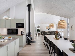 Une cuisine moderne dotée d’une cuisinière intégrée, d’un coin repas avec une longue table et des chaises, et de luminaires suspendus.