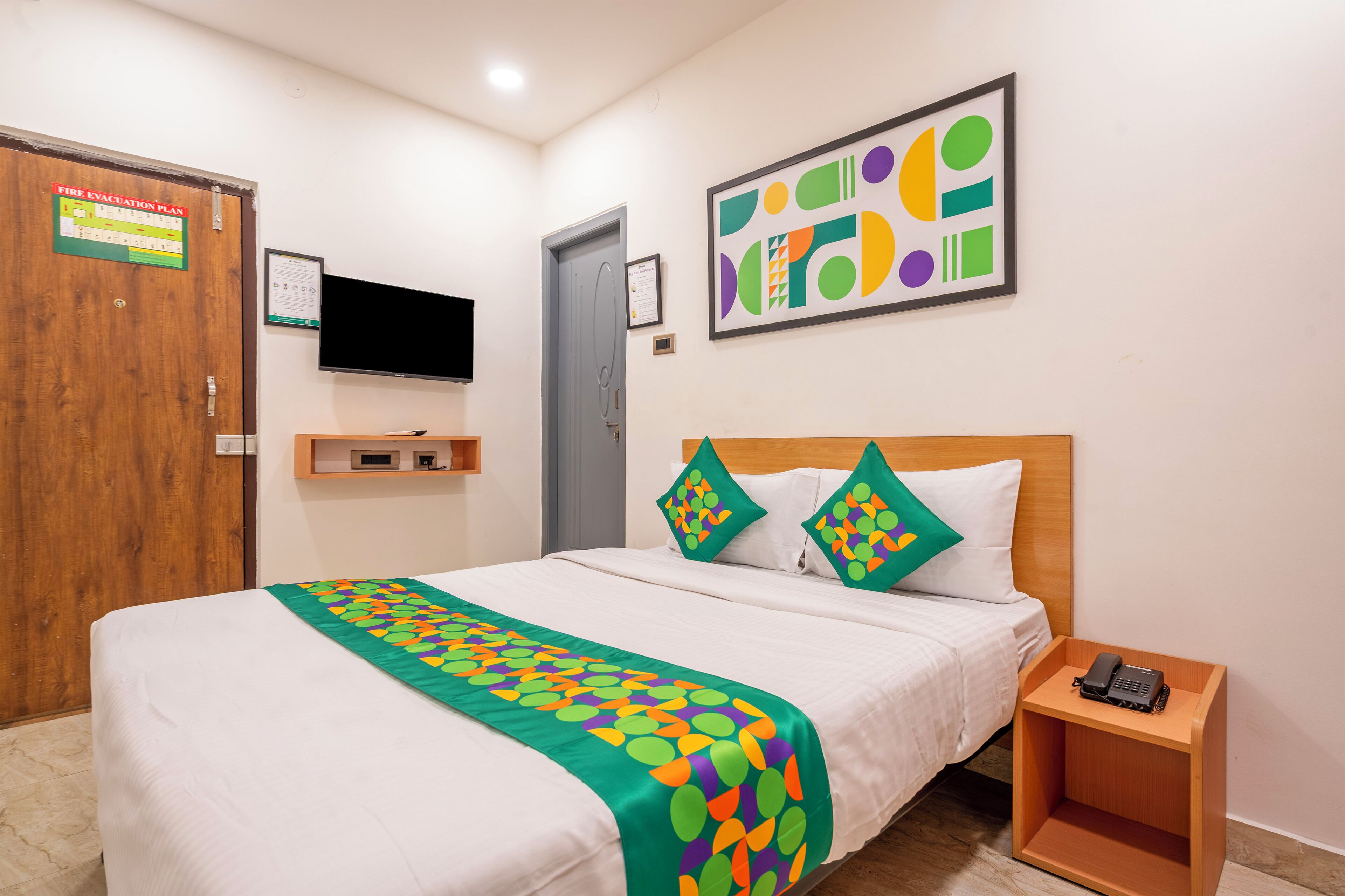 A hotel room with a bed, a wooden nightstand, a television, and a fire evacuation plan on the wall.