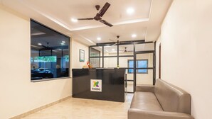 Un área de recepción con mostrador, zona de estar, ventiladores de techo y un ventanal grande.