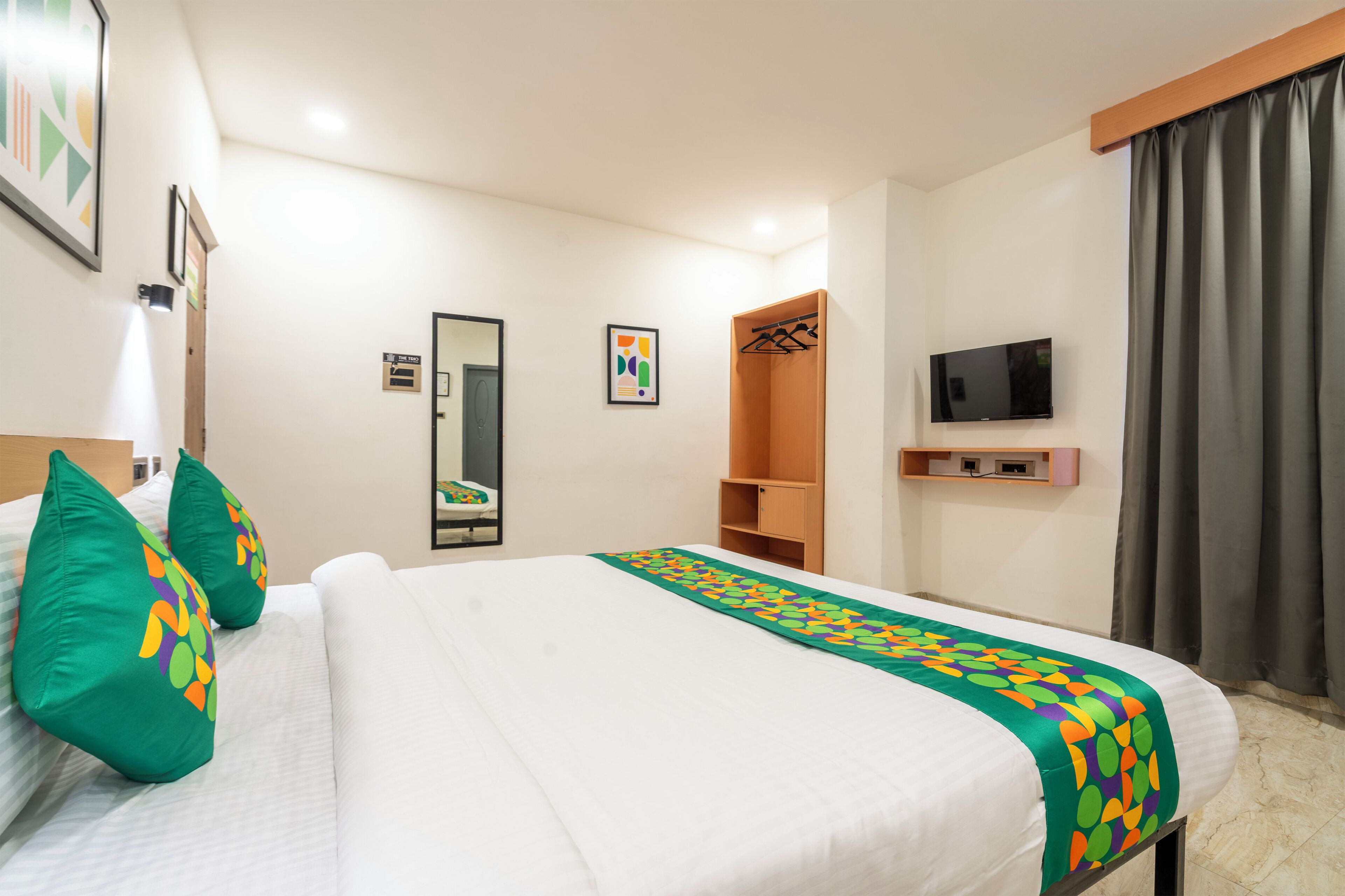 Een hotelkamer met een bed, kussens, een televisie, een kledingkast en een spiegel.