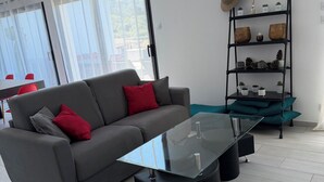 Una sala de estar moderna con un sofá gris, cojines rojos y grises, una mesa de centro de vidrio y una mesita auxiliar negra.