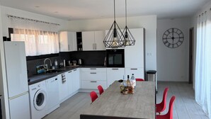 Una cocina moderna con una isla central, un comedor con sillas rojas y un reloj de pared grande.