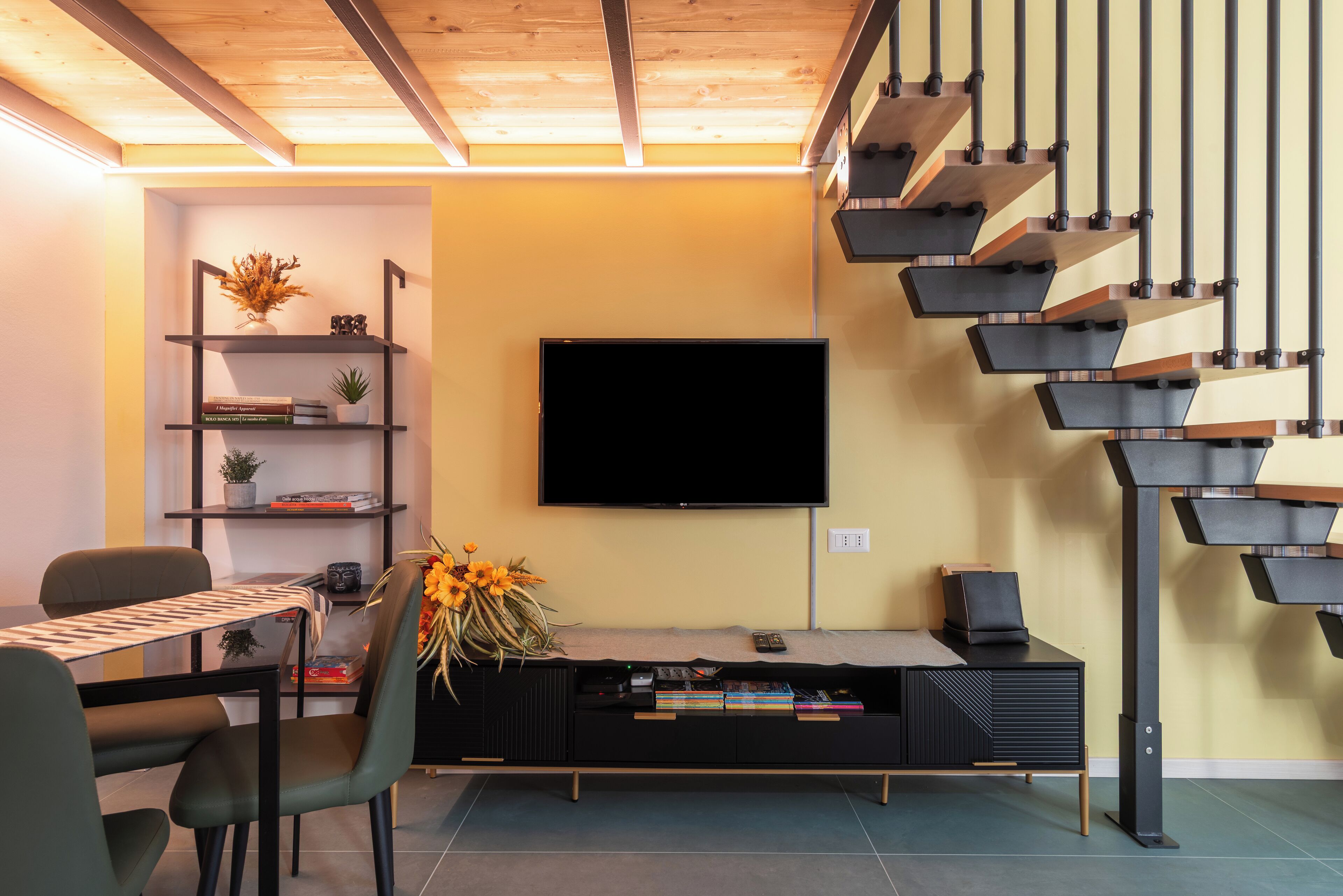 A modern living room with a flat-screen TV, a staircase, and a dining area with a table and chairs.