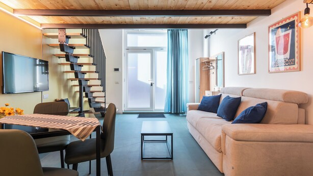 A modern living room with a sofa, a dining table, chairs, a staircase, and a television. - Modern Loft - Rho Fiera & San Siro - Milan (Milano)