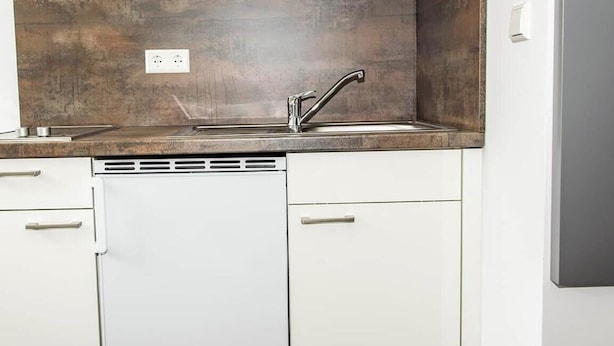 Cocina con armarios blancos, un lavamanos de acero inoxidable y una salpicadera.