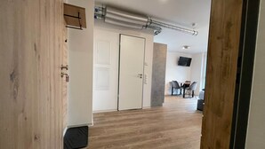 Un couloir doté d’un plancher en bois, une porte blanche et un coin repas avec des chaises et une table.