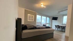 Een moderne slaapkamer met een slaapbank, een flatscreen televisie en een eethoek met stoelen en een tafel.
