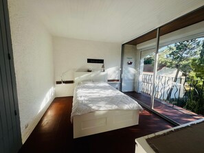 Ein Schlafzimmer mit Bett, Nachttisch, Spiegel und Blick ins Freie.