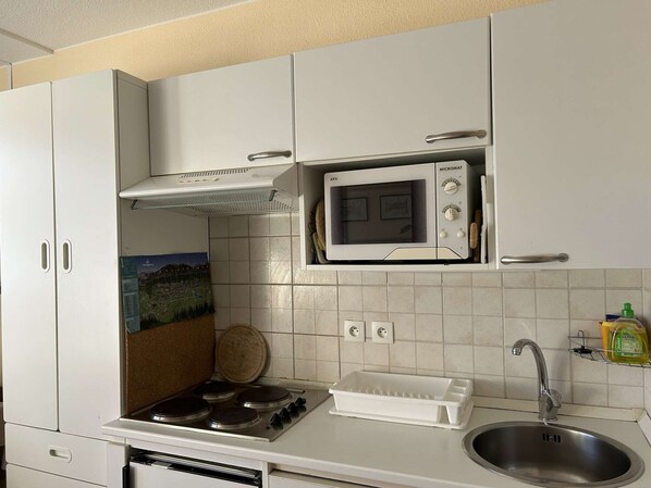 Una cocina con armarios blancos, microondas, estufa y pileta.