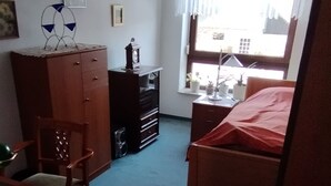 A compact hotel room with a single bed, a desk with a chair, a dresser, and a window with curtains. - Beautiful 3 room trade fair apartment (Hannover)