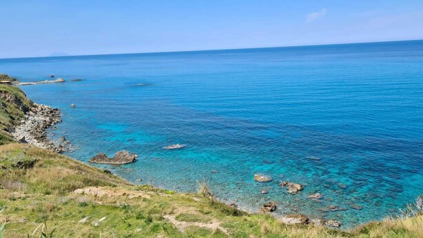 Paisaje costero con aguas azul cristalino, afloramientos rocosos y terreno cubierto de hierba.