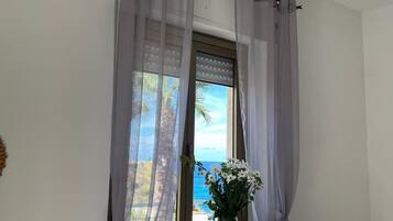 Un dormitorio con cama, mesita de noche, silla, ventana con cortinas y vista al mar.