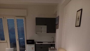 Un espacio habitable compacto con comedor, sofá, kitchenette y ventana con persianas.