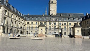 A large open square with a historic building featuring a clock tower and a tall spire.