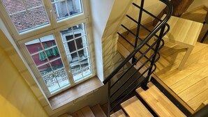 A wooden staircase with a metal handrail, leading to a landing with a window overlooking a courtyard.