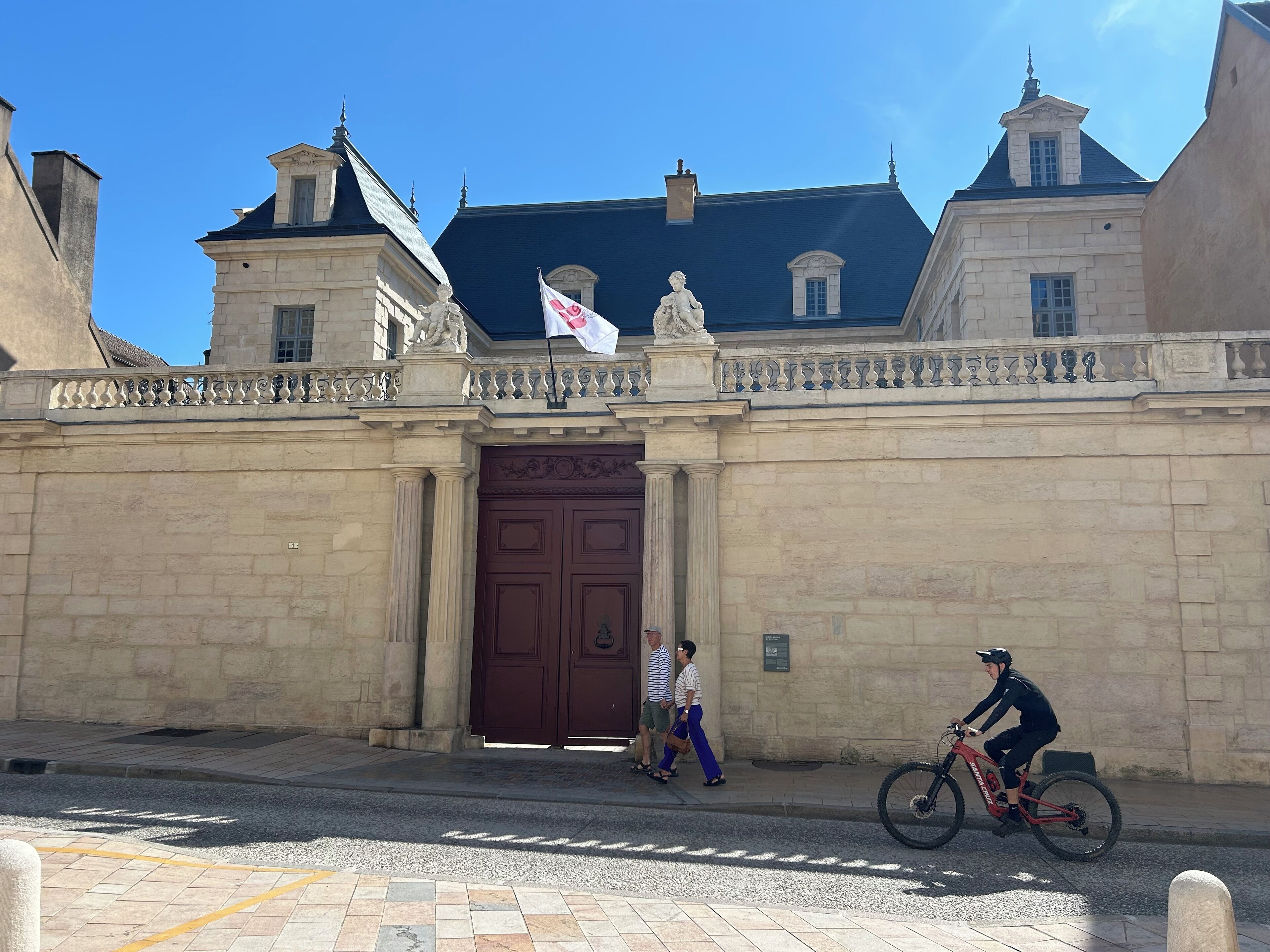 Un bâtiment historique doté d’une grande entrée centrale, d’un drapeau et d’une statue.