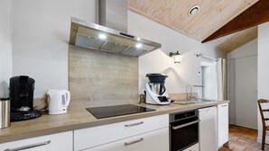 Moderni keittiö, jossa on valkoiset kaapit, puinen työtaso, sisäänrakennettu uuni ja kahvinkeitin.