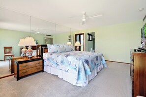 Une chambre à coucher avec un lit, une commode, un miroir et un ventilateur de plafond.
