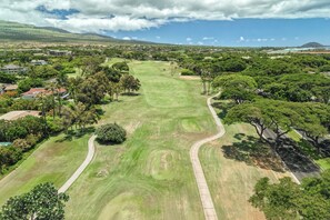 Vue aérienne d’un terrain de golf avec un chemin sinueux, entouré d’une végétation luxuriante et de bâtiments résidentiels.