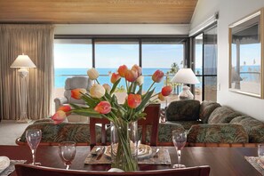 Un coin repas avec vue sur l’océan, un vase de tulipes et une table dressée pour deux personnes.