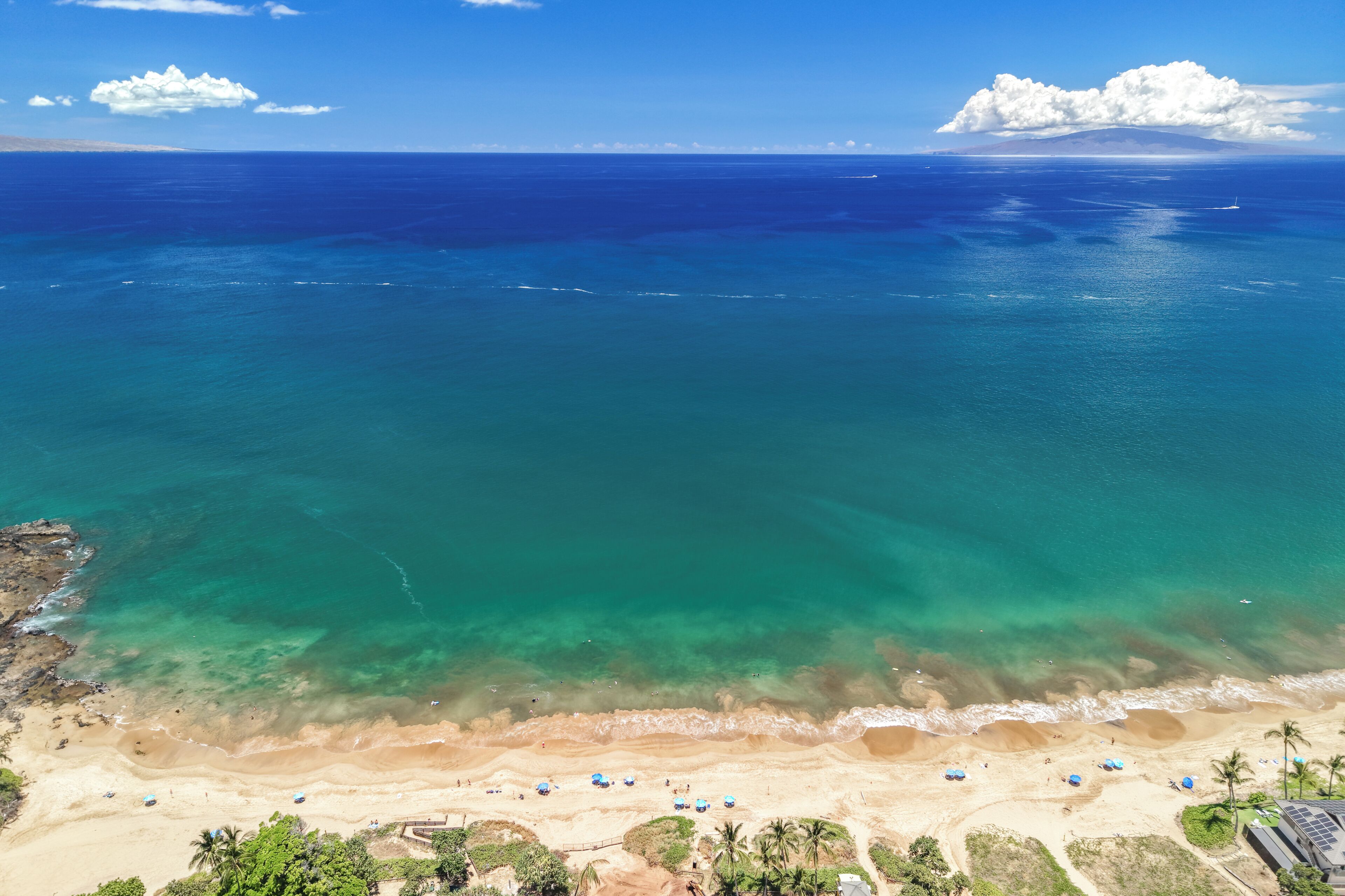 A beach with clear waters, a sandy shore, and a few umbrellas.
