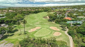 A golf course with a clear sky, surrounded by residential buildings and lush greenery. - Ocean View w/AC - Wailea Elua 306 (Kihei)