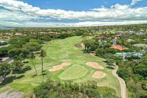 Ein Golfplatz unter blauem Himmel, umgeben von Wohngebäuden und üppiger Vegetation.