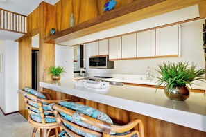Une cuisine moderne avec des meubles en bois, un îlot central, des tabourets de bar et des plantes en pot.
