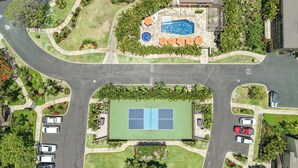 An aerial view of a residential area with a swimming pool, tennis court, and surrounding greenery. - Ocean View w/AC - Wailea Elua 306 (Kihei)